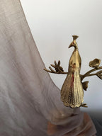 Gold peacock decorative item held against a light curtain background