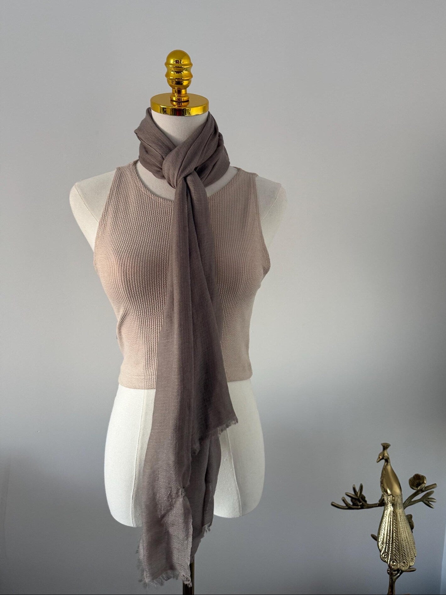Mannequin wearing a beige sleeveless top and brown scarf against a plain background