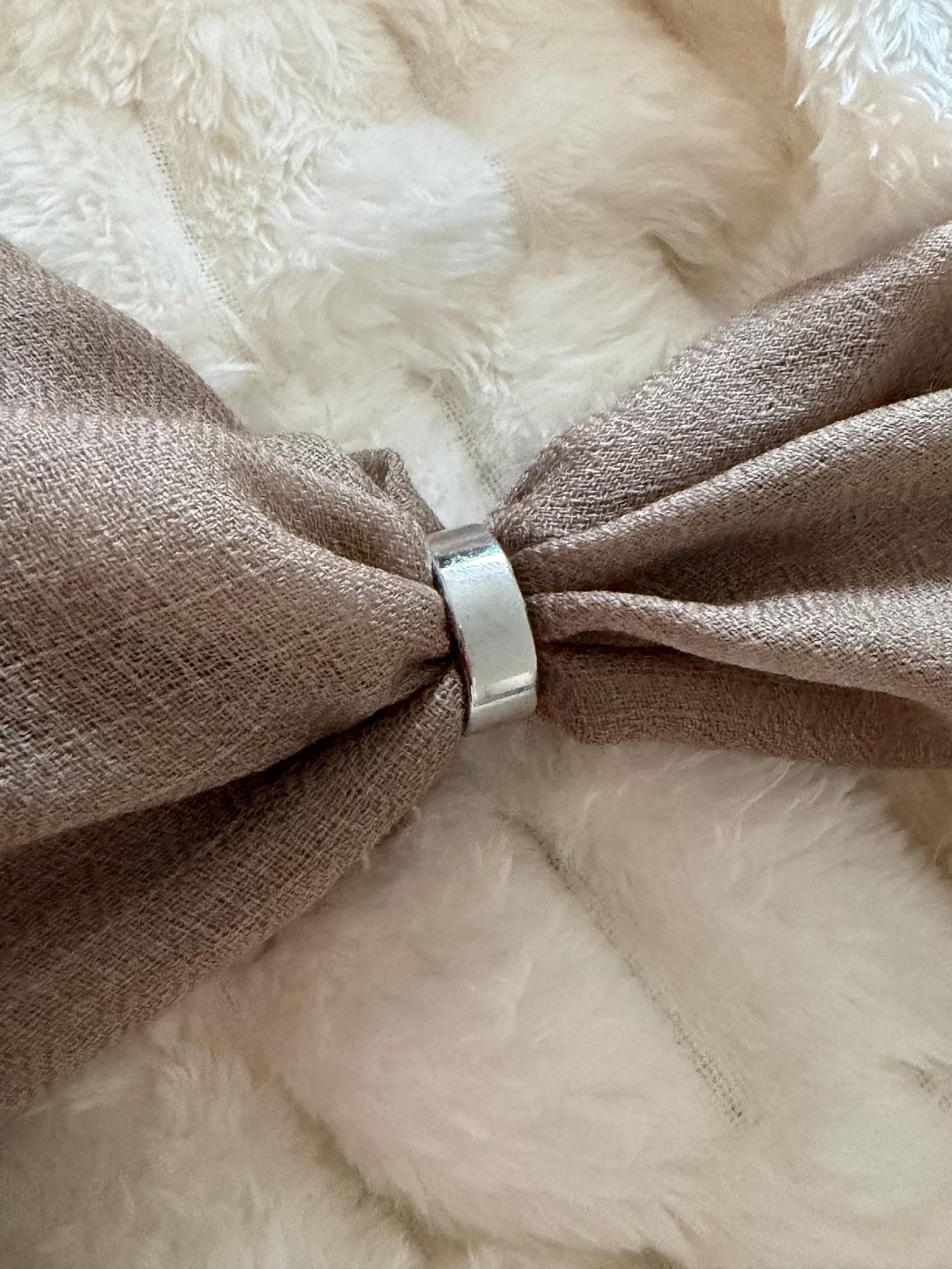 Brown fabric bow with a silver ring on a fluffy white background