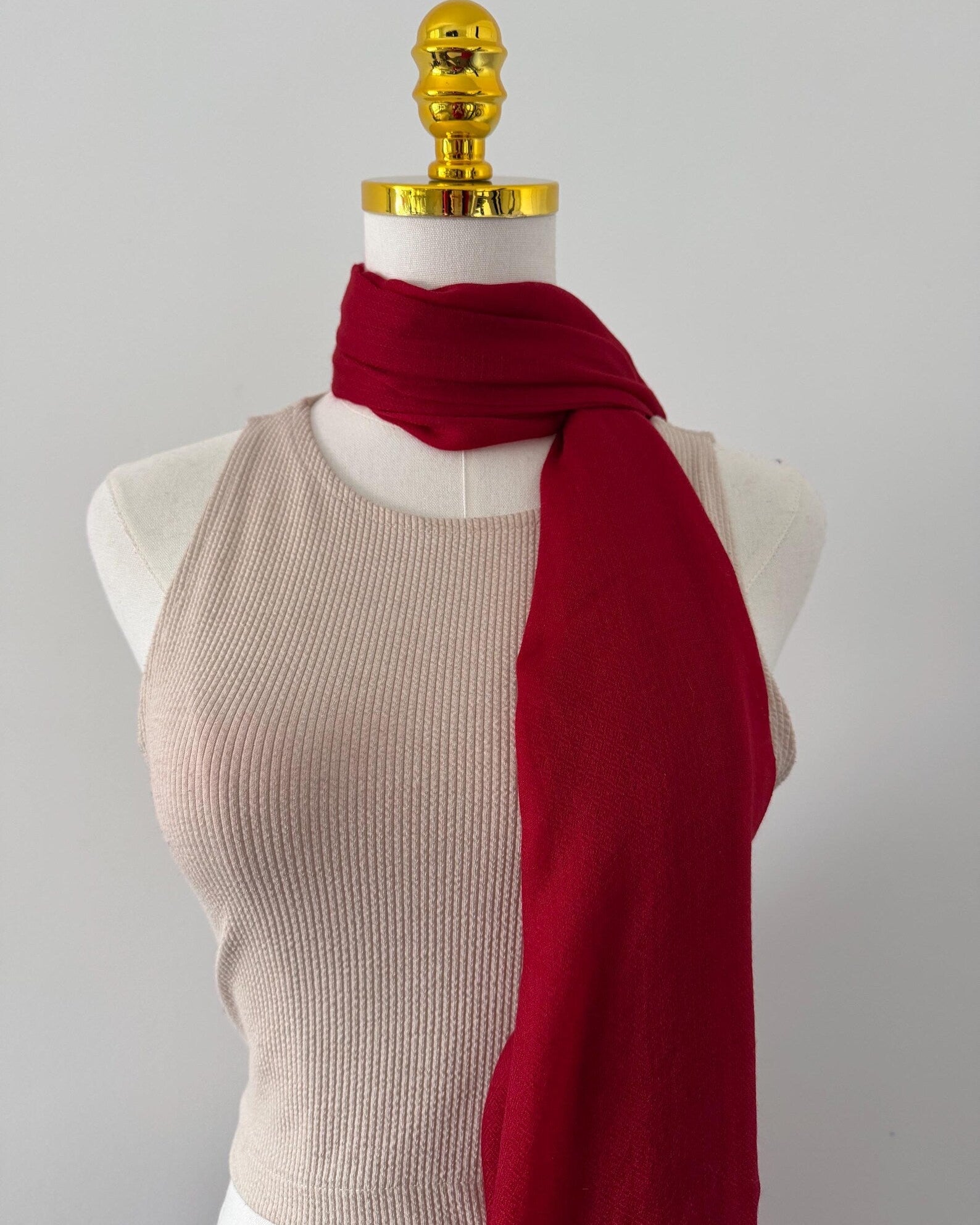 Mannequin wearing a beige ribbed top and red scarf against a plain background