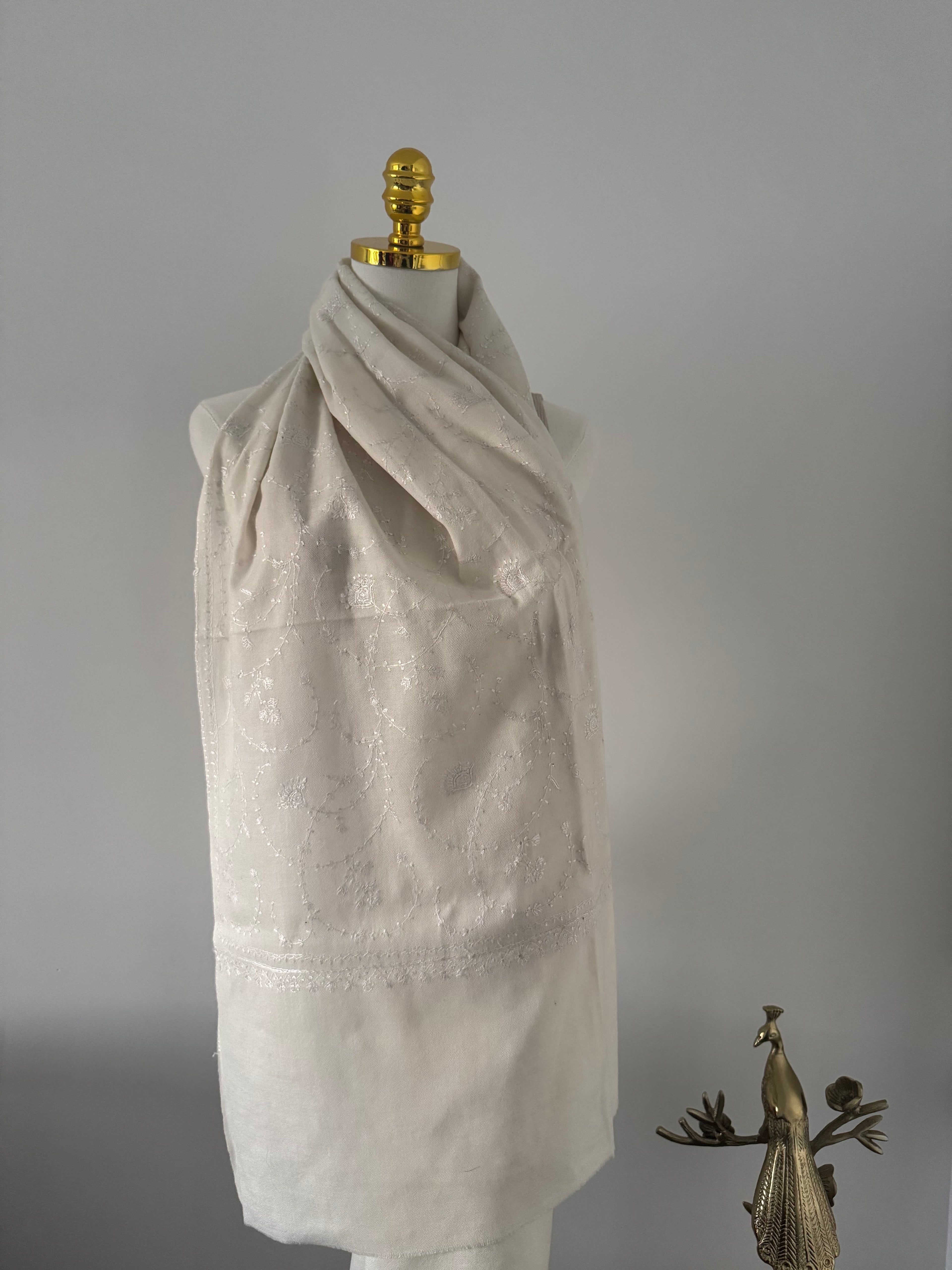 Mannequin wearing a draped garment with decorative embroidery on a plain background